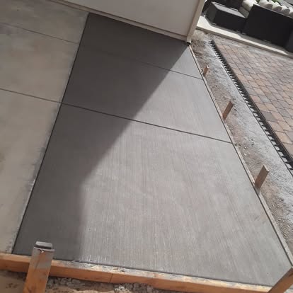 A freshly poured concrete patio with a smooth broom finish beside a paver border.